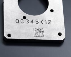Metallteil, auf dem mittels Nadelprägung eine Seriennummer und ein Datamatrix-Code eingraviert sind.